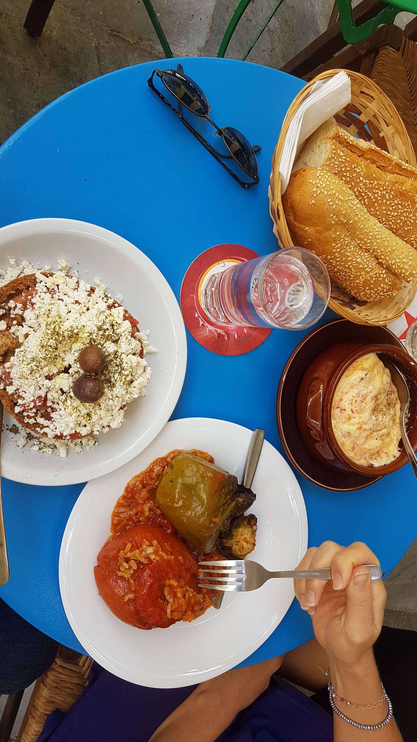 A spread of Greek taverna dishes on a blue table, including stuffed peppers and tirokafteri dip