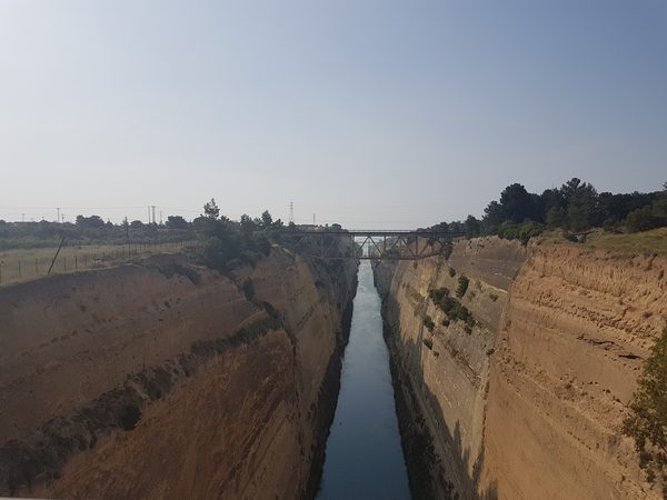 The Corinth Canal cutting a narrow straight channel between towering rock walls, seen from the bridge