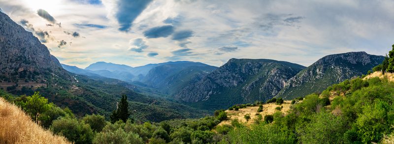 Panoramic view from Delphi over the green Pleistos Valley with ancient ruins on the hillside and olive groves stretching to the Gulf of Corinth in spring morning light