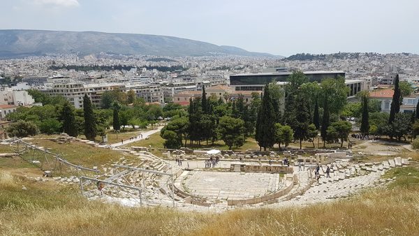 The ruins of an ancient theatre on the south slope of the Acropolis, with the Acropolis Museum and the Athens skyline in the background
