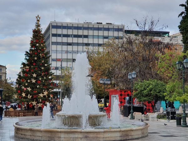 People in winter coats around the fountain in Syntagma Square under a grey December sky